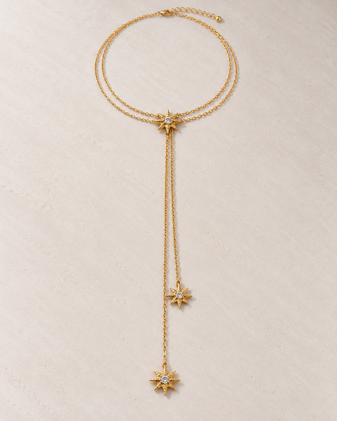 Collar Céleste lariat con estrellas doradas sobre cemento blanco
