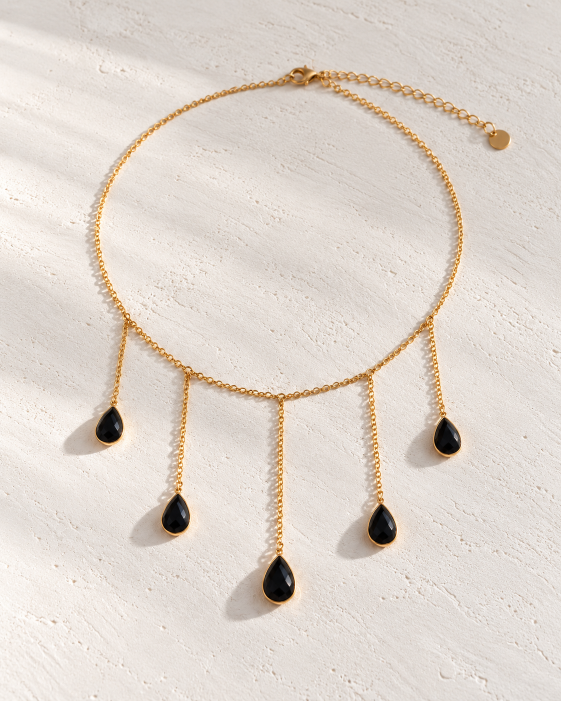 Collar Octavia dorado con lágrimas negras sobre cemento blanco